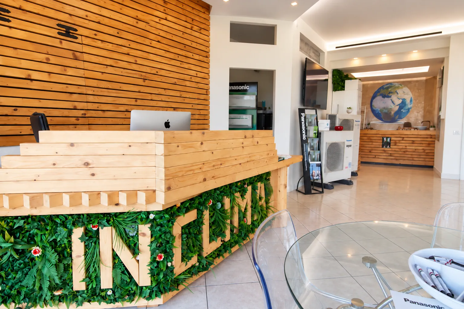 Il banco accoglienza in legno con la scritta IN CLIMA, tavolo in vetro e unità Panasonic esposte